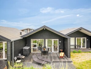 A modern house with a patio area featuring a table, chairs, and lounge chairs.