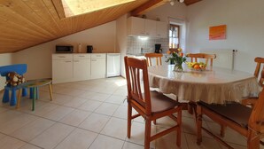 A dining area with a wooden table and chairs, a kitchen in the background, and a sloped ceiling with a skylight. - Ferienwohnung 1 im DG für 1-5 Personen (Bernau am Chiemsee)