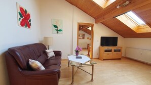A cozy living room with a brown leather couch, a glass coffee table, and a wooden cabinet with a television. - Ferienwohnung 1 im DG für 1-5 Personen (Bernau am Chiemsee)