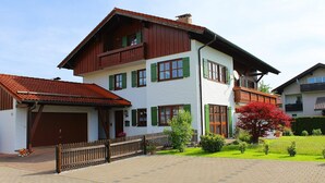 A two-story house with a balcony, a garage, and a well-maintained garden. - Ferienwohnung 1 im DG für 1-5 Personen (Bernau am Chiemsee)