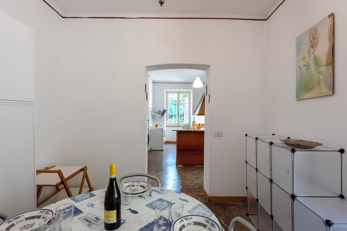 A dining area with a table set for two, a bottle of wine, and a painting on the wall.