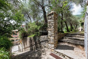 A stone staircase leading up to a building with a metal railing, surrounded by trees and greenery. - Mulinetti Houses (Recco)