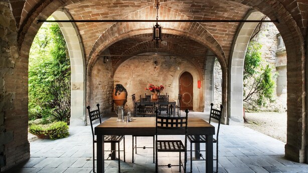 Un espace de restauration en plein air agrémenté d’une arche en briques, de murs en pierre et d’une table dressée pour quatre personnes.