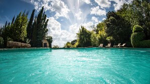 Une piscine d’un bleu éclatant, dotée de chaises longues et bordée d’un côté par un mur de pierre.