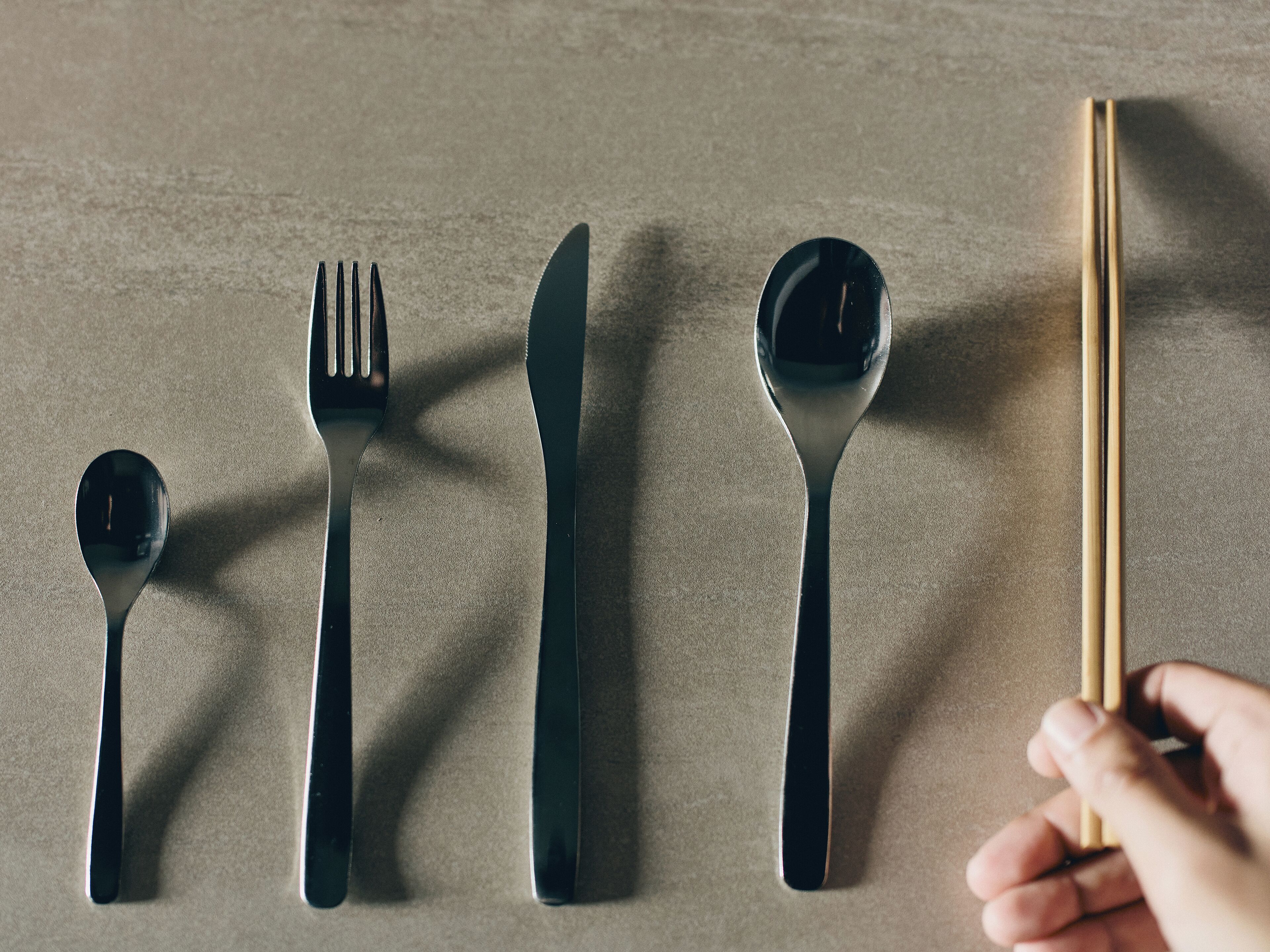 A set of black cutlery including a spoon, fork, knife, and chopsticks, arranged on a textured surface.