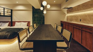 A modern hotel room with a large wooden dining table, comfortable seating, a bunk bed, and a kitchenette. - illi Tas Shinjuku (Tokyo)