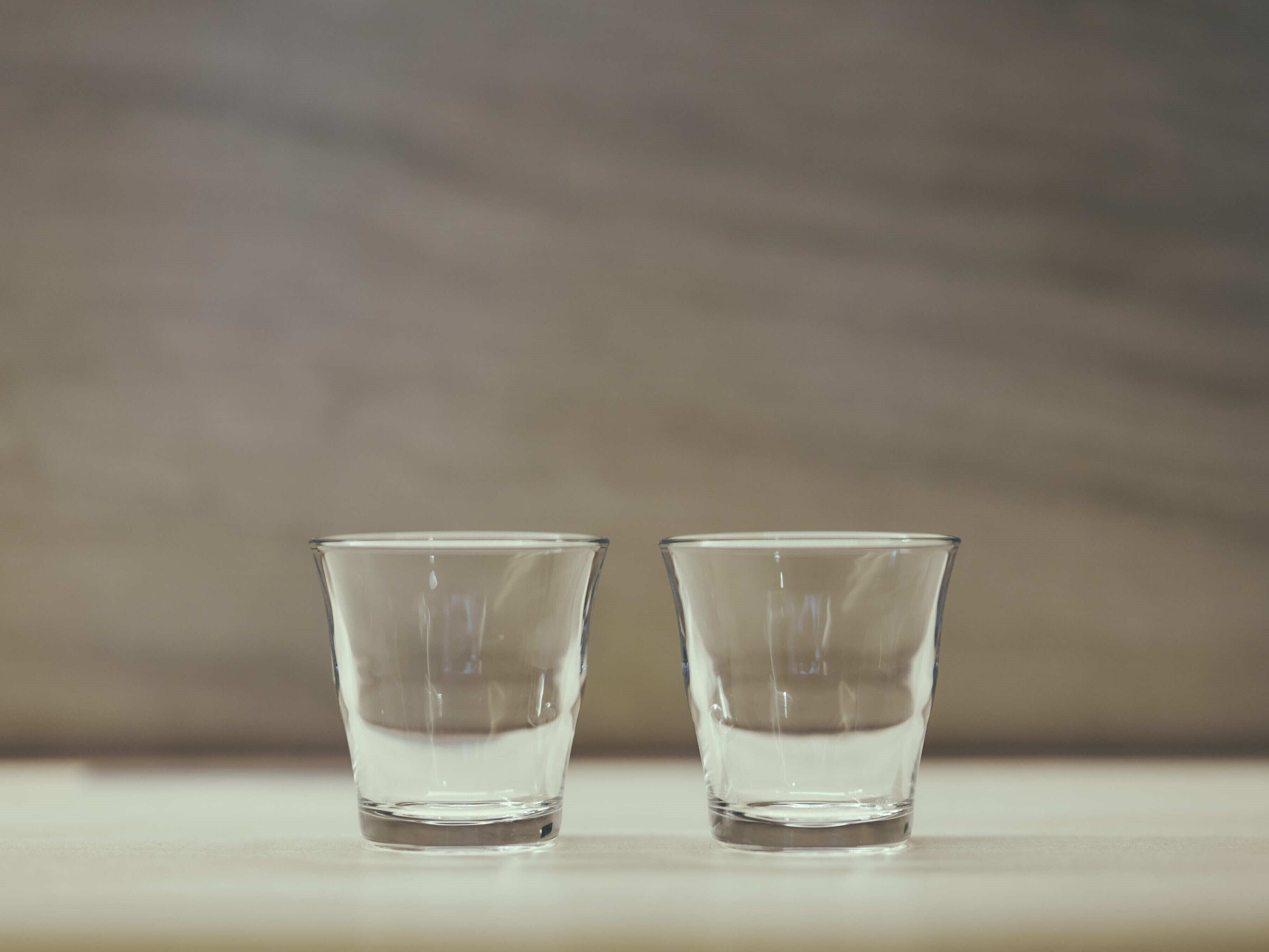 Two clear glasses on a flat surface with a neutral background.