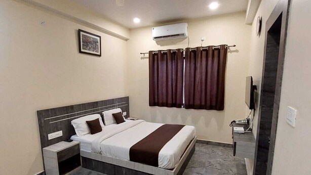Un dormitorio con cama, mesita de noche, equipo de aire acondicionado, ventilador de techo y baño con espejo y toallero.