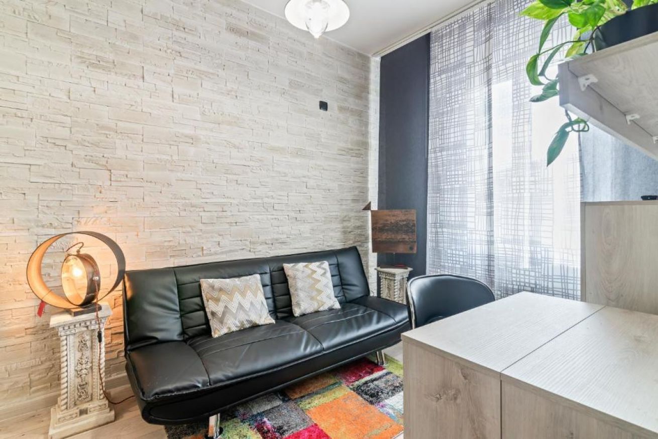 Un salon moderne avec un canapé en cuir noir, une petite table, une lampe décorative et une plante.