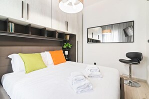 Habitación de hotel moderna con una cama grande, una mesita de noche con lámpara, un espejo y una silla negra.
