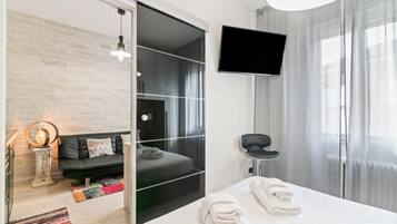 A modern hotel room with a bed, a sofa, a TV, and a sliding door leading to a balcony.