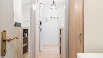 A narrow hallway with a wooden door on the left, a white wall with a light fixture, and a white door on the right.