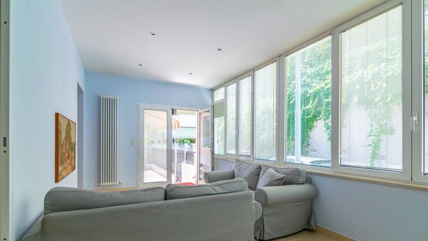 A living room with a grey sofa, a radiator, and large windows. - GuestHost - Comfortable apartment located on the ground floor of a renovated building.In 110 m2 of space, it comfortably accommodates 4 people with two double bedrooms and two bathrooms.Possibility to park for free inside the property, in the courtyard ( (Rimini)