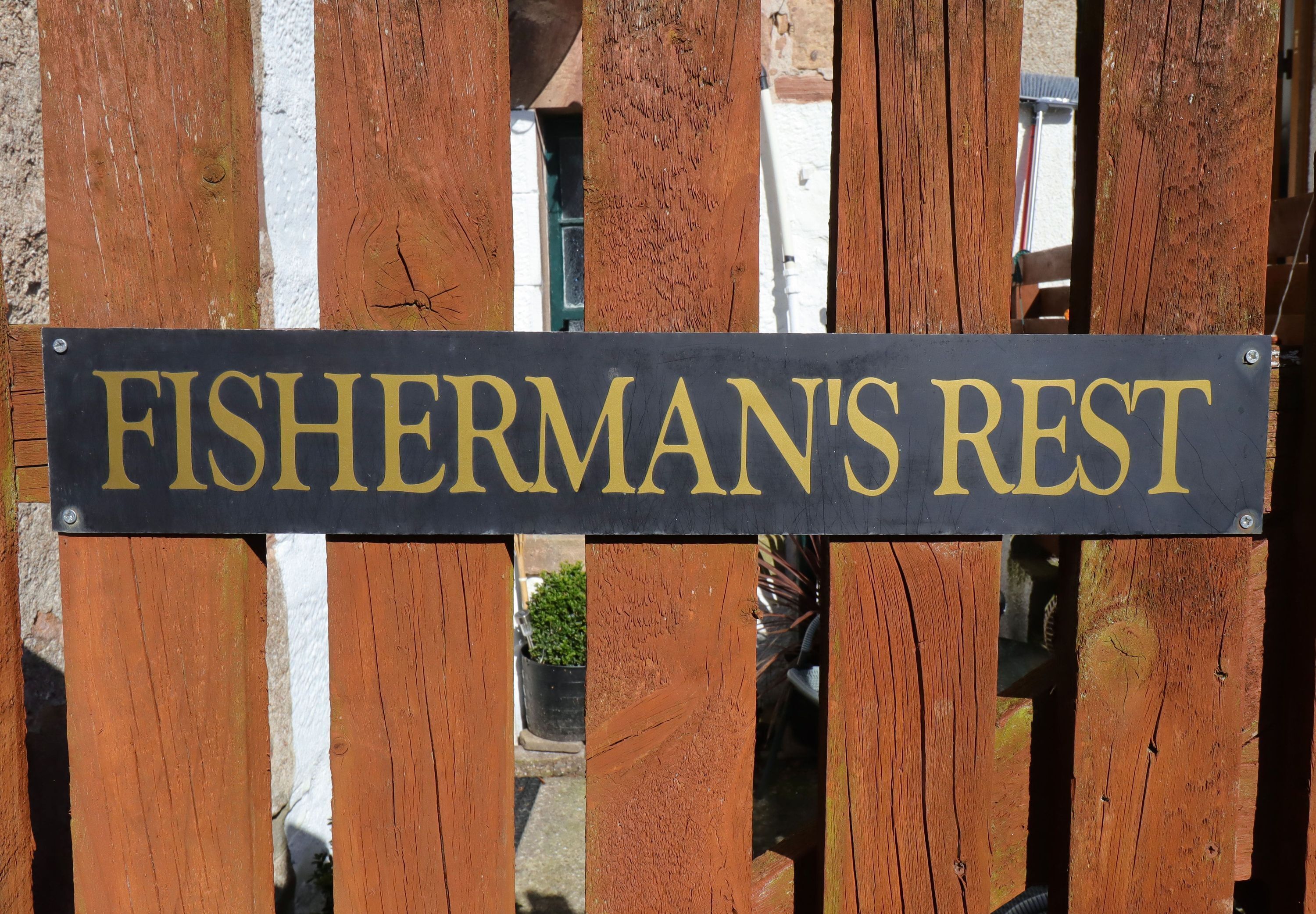 A sign that reads "FISHERMAN'S REST" mounted on a wooden fence.