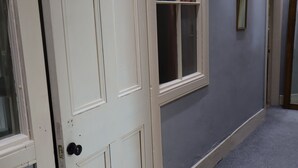 Ένας διάδρομος με μια λευκή πόρτα, ένα παράθυρο με κουρτίνα και ένα γκρι χαλί.