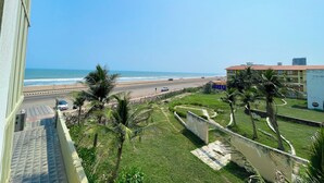 A view of a beach from a balcony, with a road and palm trees in the foreground. - TBS Sea View - Full AC- Pool & Breakfast (Puri)