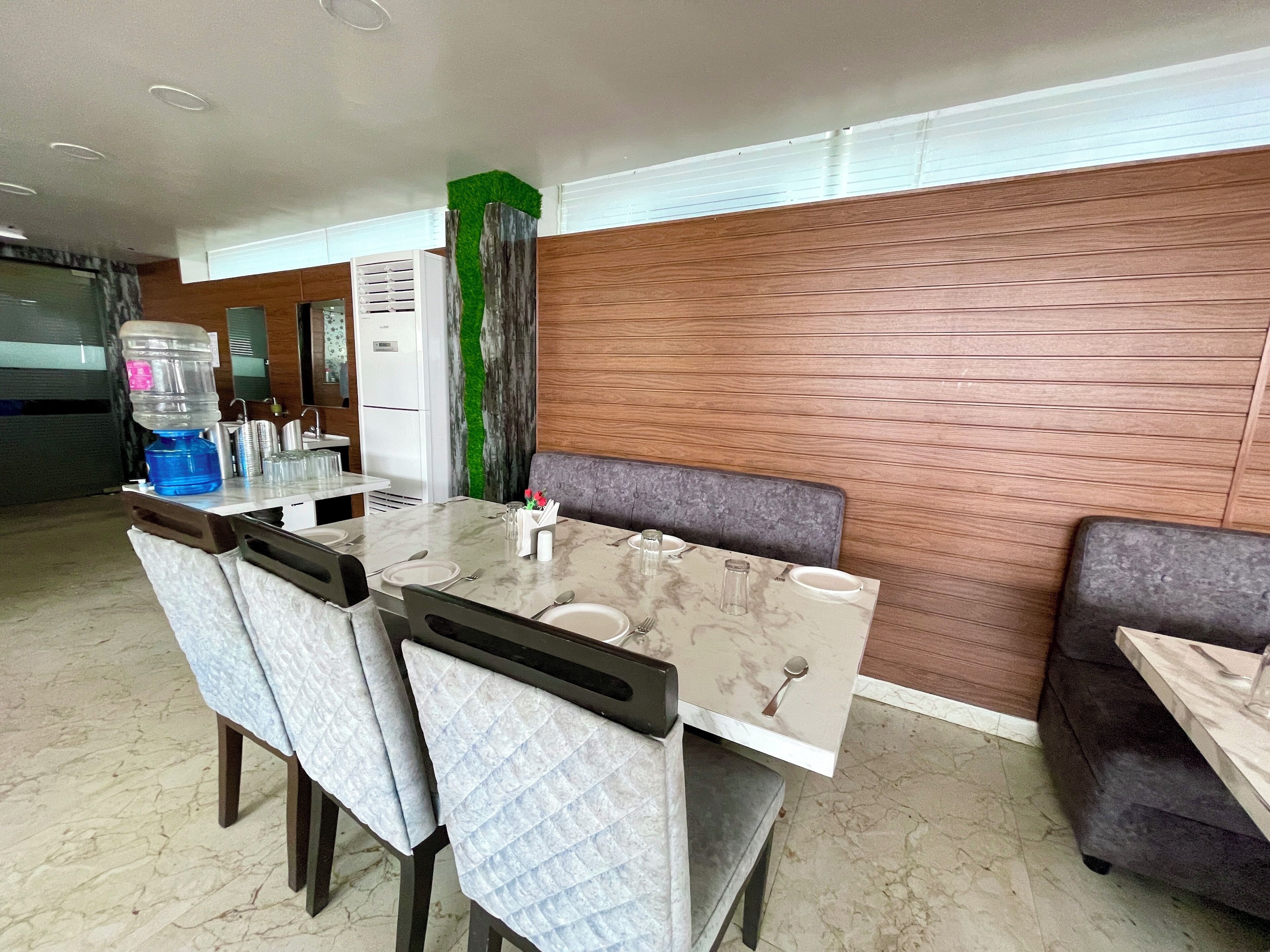 Un comedor con una mesa de mármol, sillas acolchadas, dispensador de agua y refrigerador.