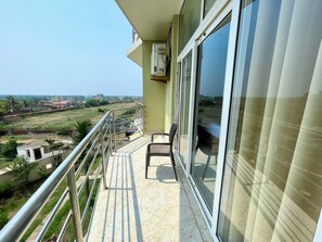 A balcony with a view of a green landscape and buildings in the distance. - TBS Sea View - Full AC- Pool & Breakfast (Puri)