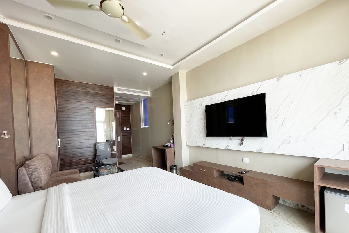 Quarto de hotel moderno com uma cama grande, uma TV presa a uma parede de mármore, uma escrivaninha com uma cadeira e um guarda-roupa.