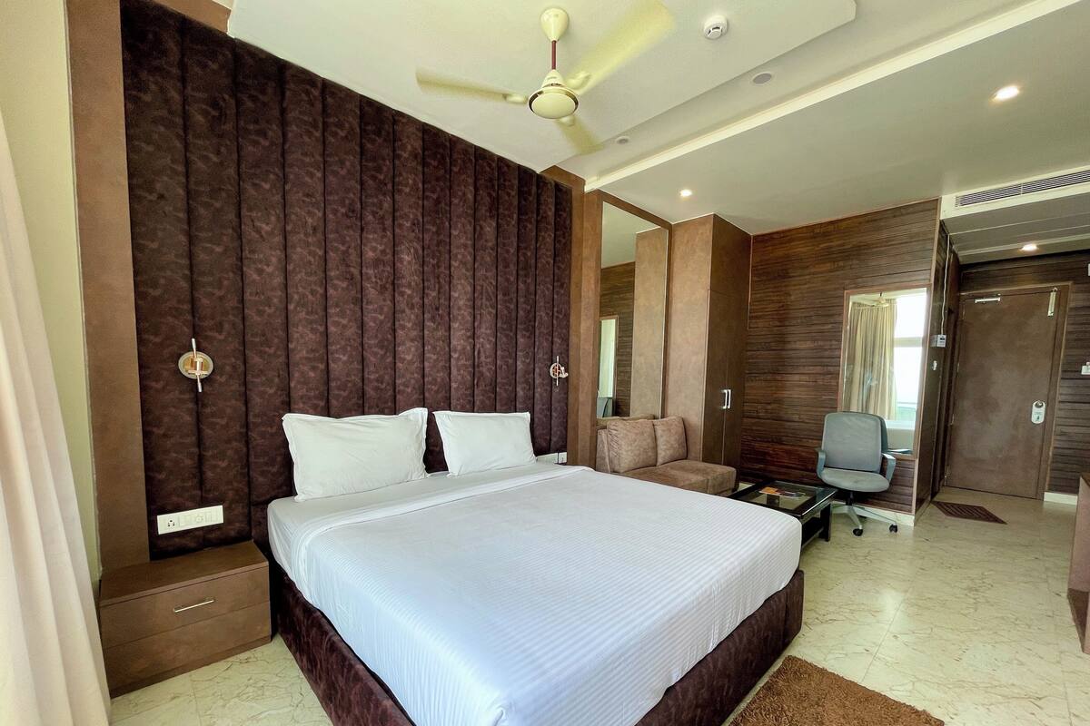 Um quarto moderno com uma cama grande, um ventilador de teto, uma escrivaninha com cadeira e um guarda-roupa.