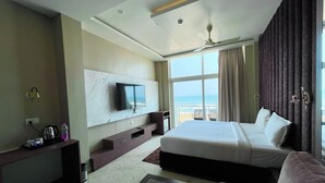 A hotel room with a large bed, a TV mounted on the wall, a ceiling fan, and a view of the ocean. - TBS Sea View - Full AC- Pool & Breakfast (Puri)