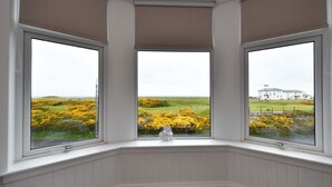 A bay window with three panes, offering a view of a white building and a landscape with yellow flowers. - Arran View in Prestwick (Prestwick)
