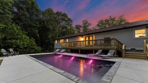 A modern house with a swimming pool, deck chairs, and a wooden deck. - Lakefront Retreat with Private Dock, Pool, Game Room | Sleeps 18 (Mooresville)