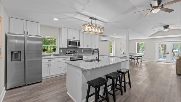 A modern kitchen with a central island, stainless steel appliances, and a ceiling fan. - Lakefront Retreat with Private Dock, Pool, Game Room | Sleeps 18 (Mooresville)