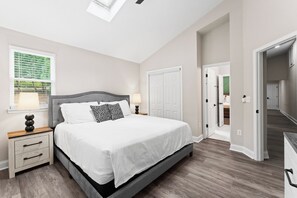A bedroom with a bed, nightstands, a window with blinds, and a door leading to another room. - Lakefront Retreat with Private Dock, Pool, Game Room | Sleeps 18 (Mooresville)