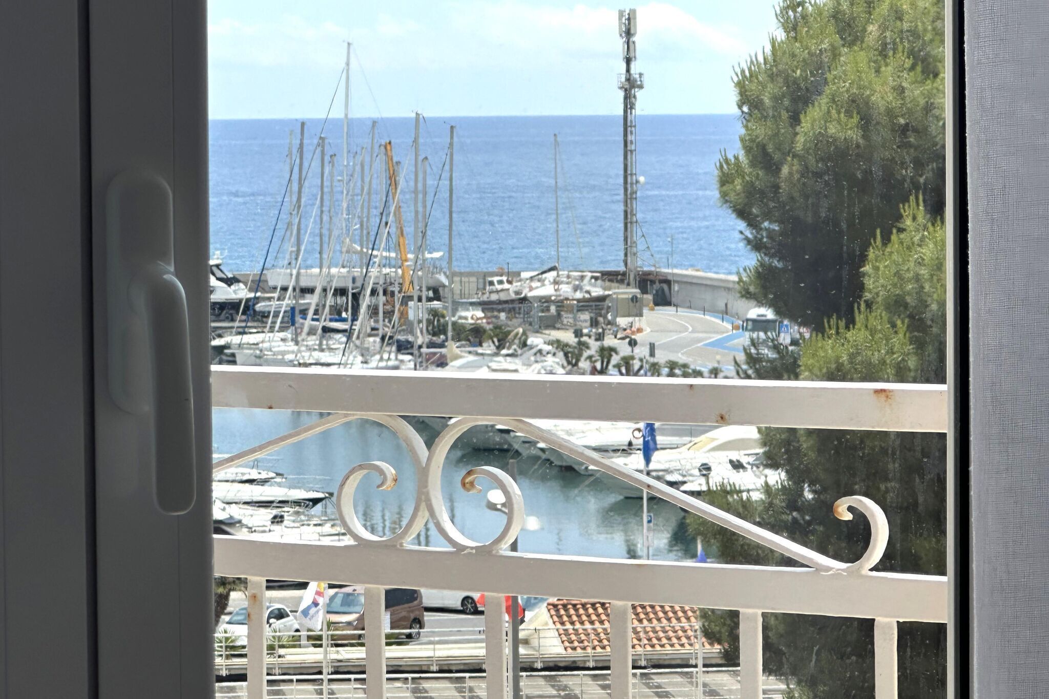 A marina with boats docked, a clear view of the sea, and a balcony railing.