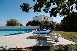 A swimming pool with lounge chairs, a clear sky, and a building in the background.