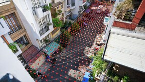 Vista de calle con faroles rojos colgados sobre el camino, edificios con balcones y un letrero que dice 'PHO'.