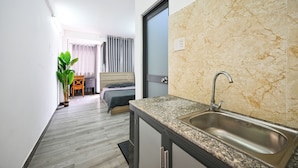 Cocina moderna con encimera de granito y pileta de acero inoxidable, un dormitorio con cama y cortinas, y un pasillo con una planta en maceta.
