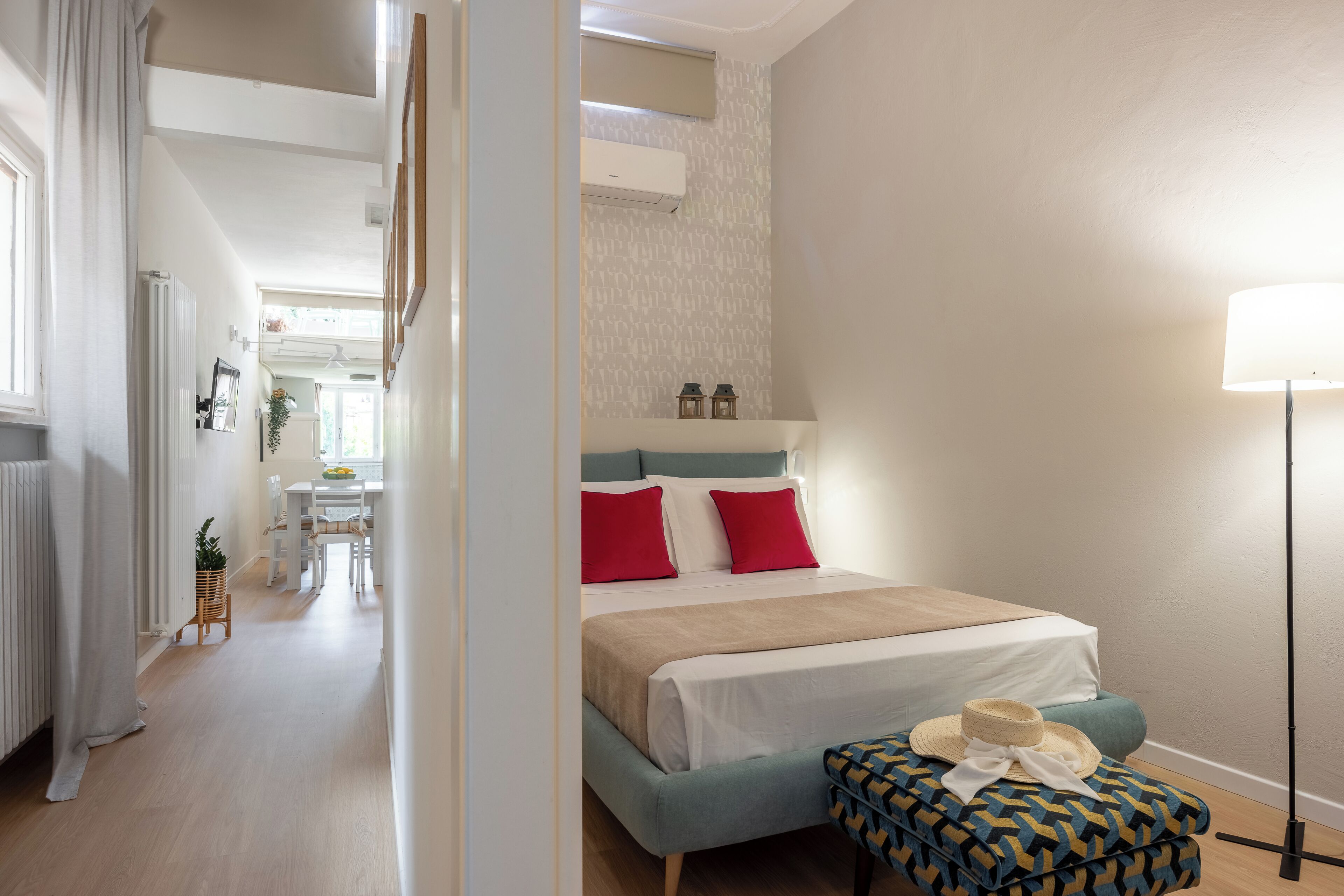 A bedroom with a bed, bedside table, lamp, and a view of the hallway.