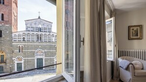 Ein Zimmer mit Fenster und Blick auf ein historisches Gebäude, einem Heizkörper und einem gerahmten Bild an der Wand.
