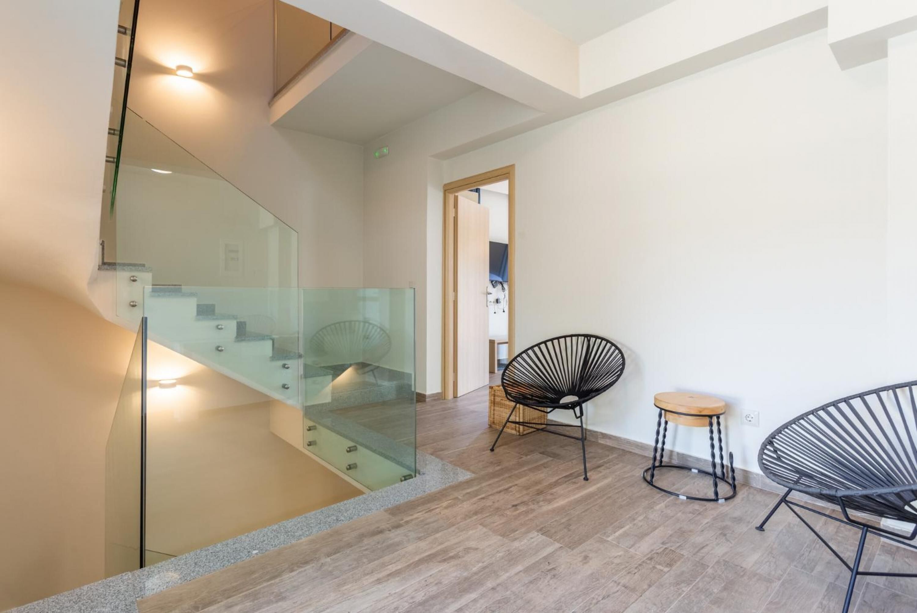 A modern interior with a glass staircase, wooden flooring, and contemporary chairs.