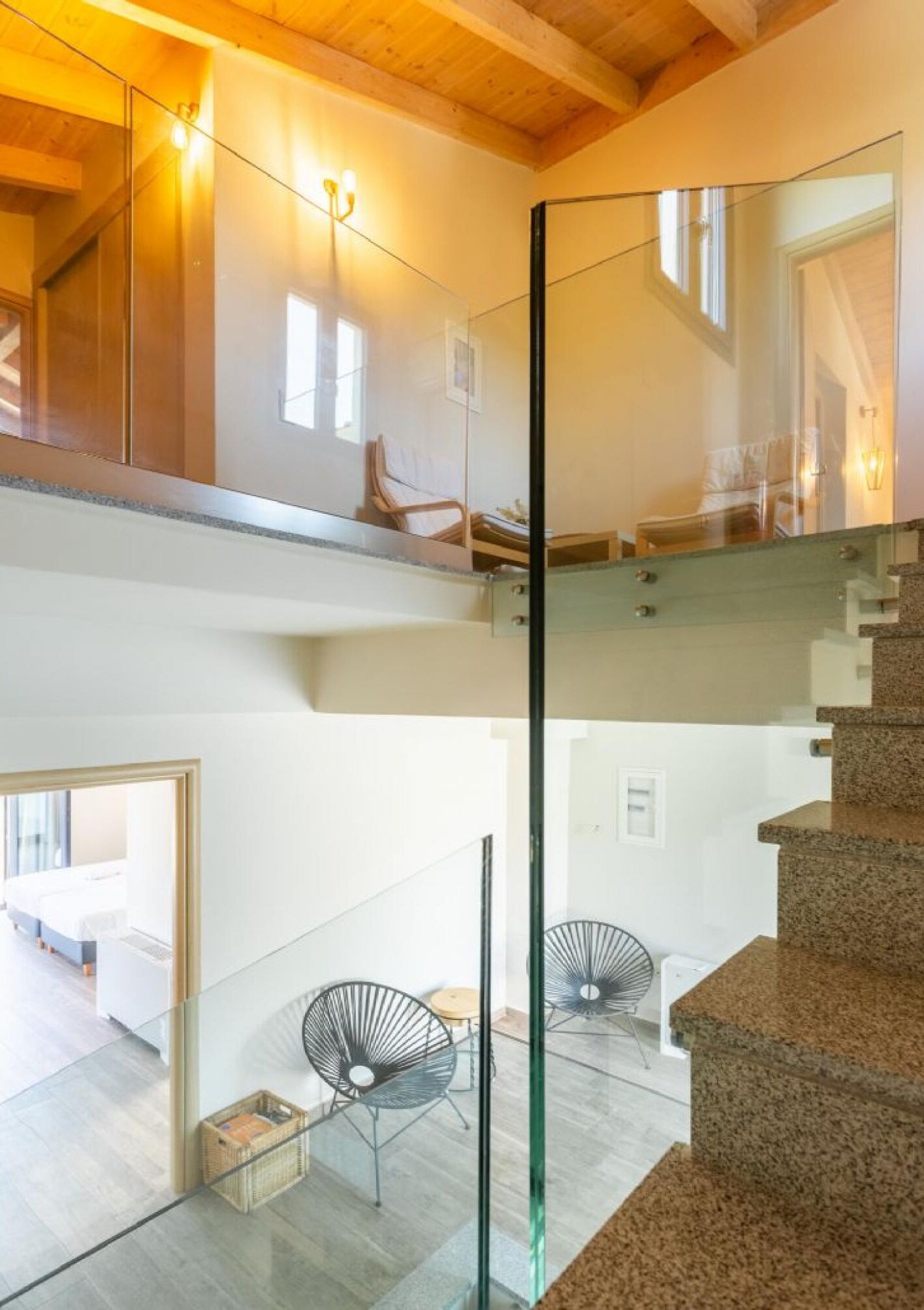 A modern interior with a glass staircase, a high ceiling, and a seating area with chairs.