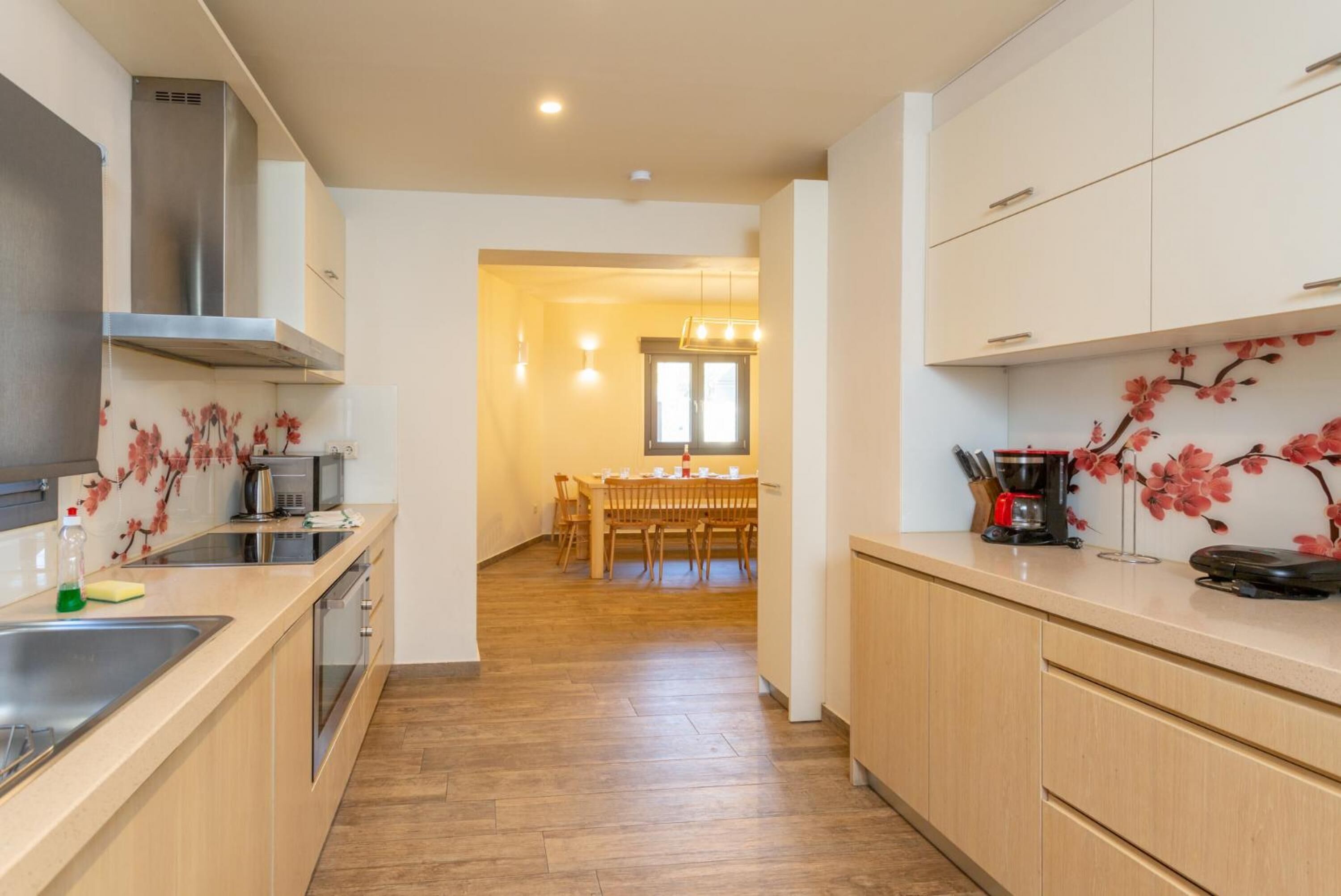 A modern kitchen with wooden cabinets, a stainless steel range hood, and a dining area with a wooden table and chairs.