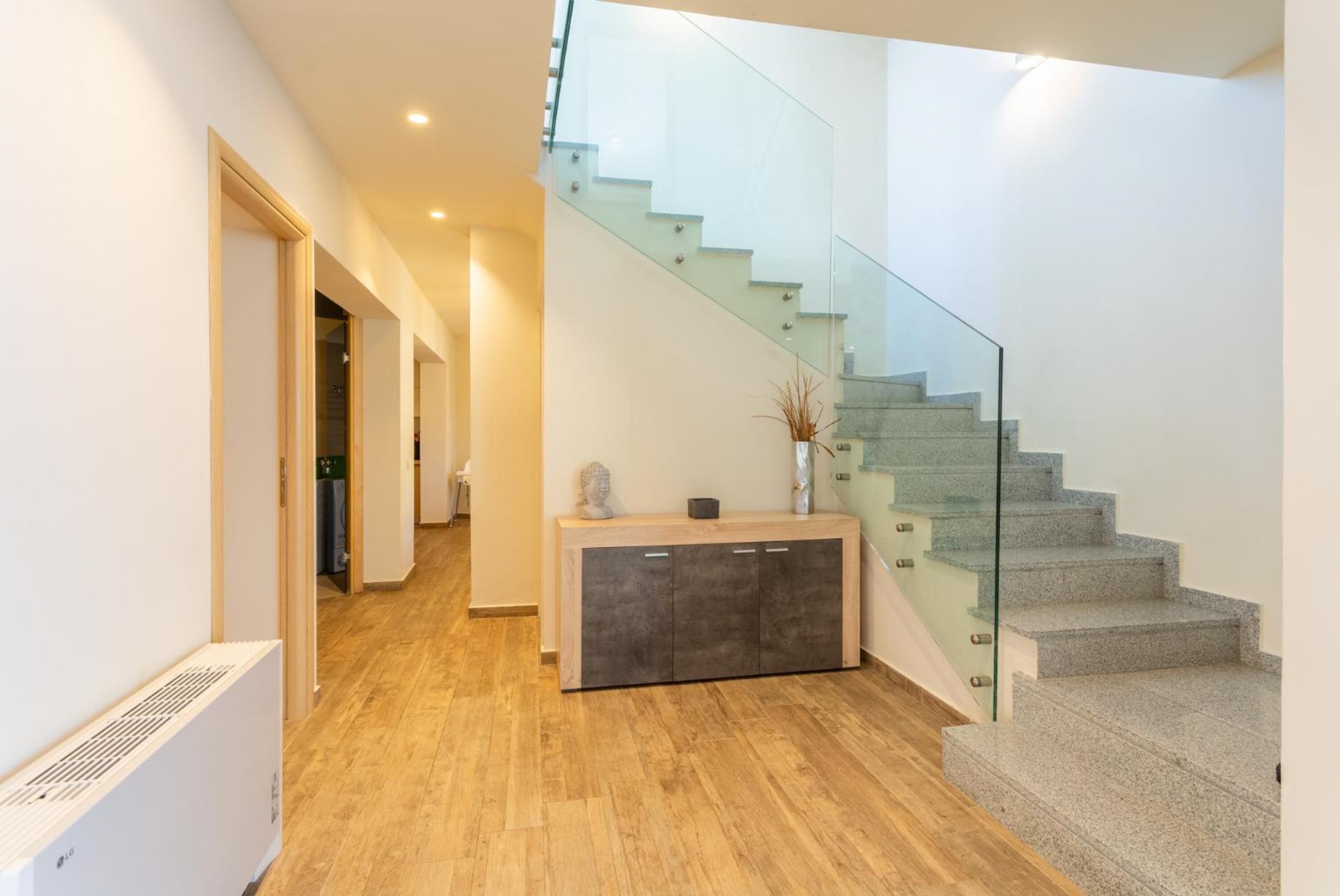 A modern interior with a staircase, a wooden floor, and a glass railing.