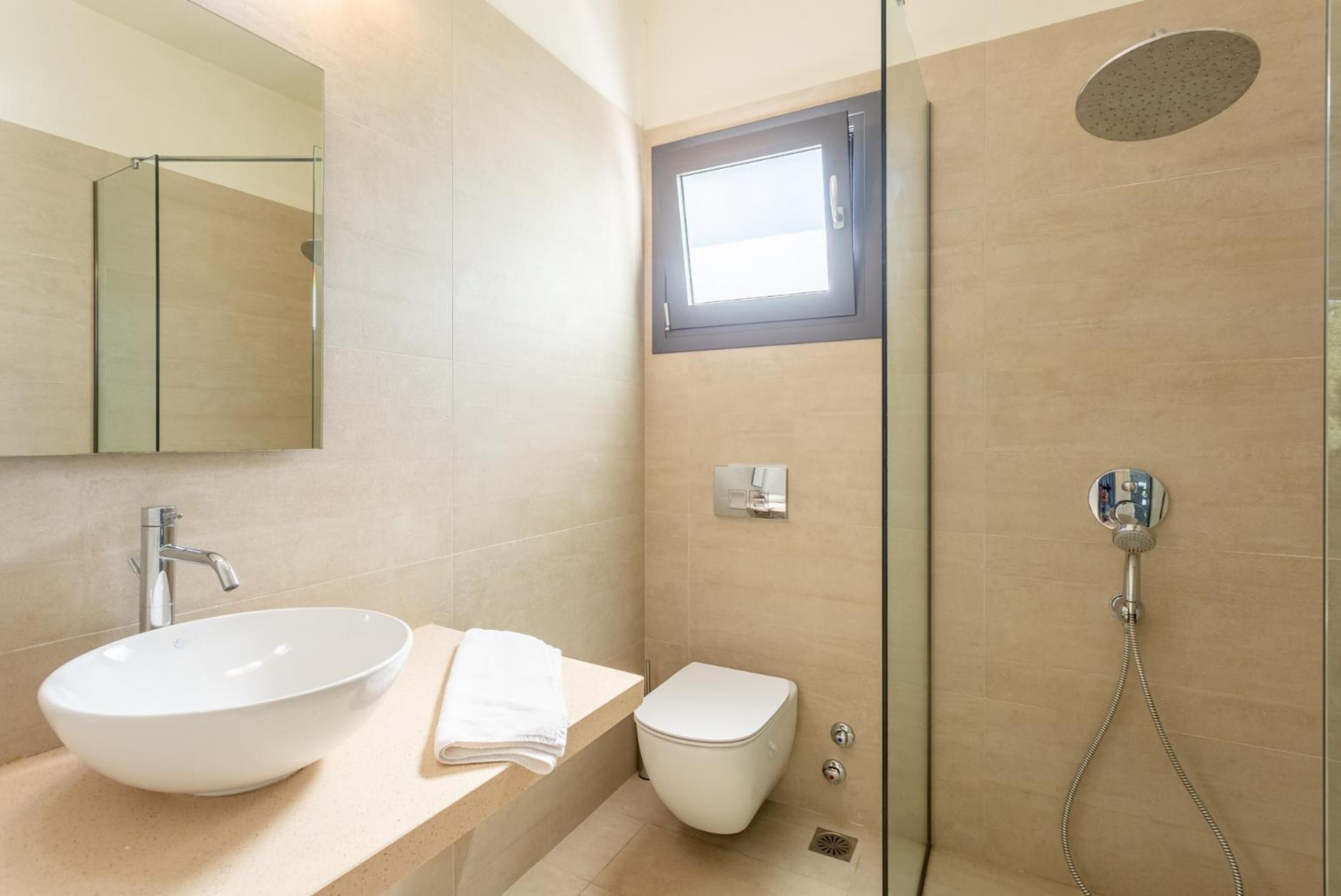 A modern bathroom with a large white sink, a toilet, and a shower with a handheld showerhead.