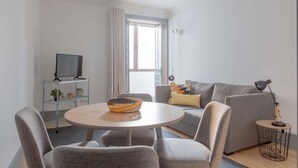 A modern living room with a round table, grey sofa, and a TV on a shelf.
