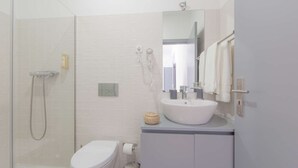 A modern bathroom with a glass shower enclosure, a white toilet, a sink with a mirror above it, and a towel rack.