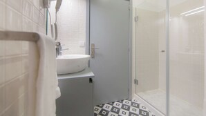 A bathroom with a white sink, a hairdryer, and a shower with a glass door. - Studio with Mezzanine (Porto)