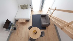A modern loft-style bedroom with a loft bed, a gray sofa, a small round table, and a wooden staircase. - Studio with Mezzanine (Porto)