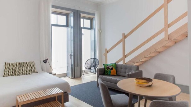 A modern hotel room with a bed, a sofa, a dining table, and a staircase. - Studio with Mezzanine (Porto)