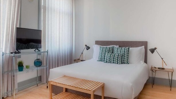 Ein ordentlich eingerichtetes Schlafzimmer mit einem Bett, Nachttischen, einem Fernseher und einer kleinen Bank.