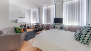 Ein Hotelzimmer mit Bett, Sofa, Schreibtisch, Fernseher und Vorhängen.