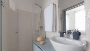Ein modernes Badezimmer mit einer Duschkabine aus Glas, einem weißen Waschbecken und einem Spiegel darüber.