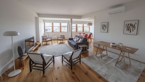 Una sala de estar amplia con un gran ventanal, un sofá, dos sillones, una mesa de comedor y una mesa de centro.