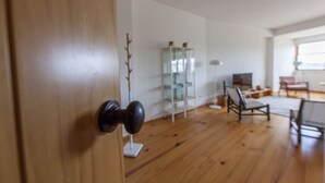 Una puerta de madera con un pomo negro, un estante de vidrio, un televisor y una silla en una habitación con suelo de madera.